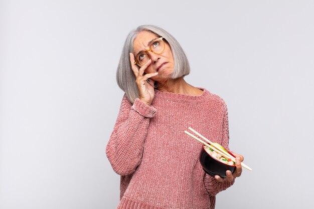 Middle age woman feeling bored, frustrated and sleepy after a tiresome, dull and tedious task, holding face with hand asian food concept