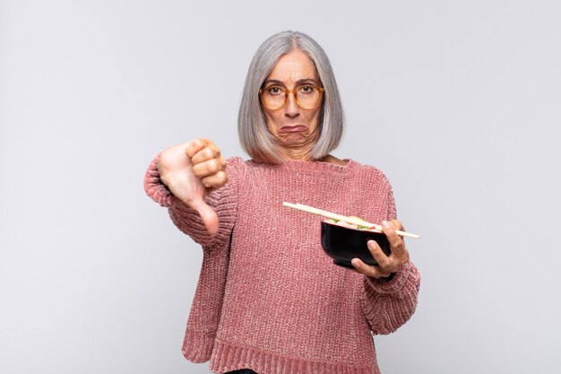 Middle age woman feeling cross, angry, annoyed, disappointed or displeased, showing thumbs down with a serious look asian food concept