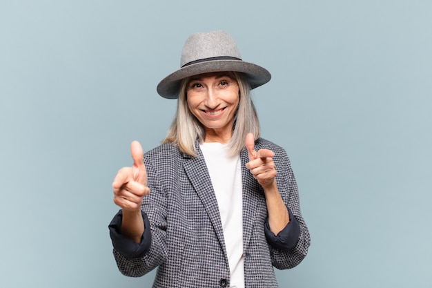 Middle age woman feeling happy, cool, satisfied, relaxed and successful, pointing at camera, choosing you