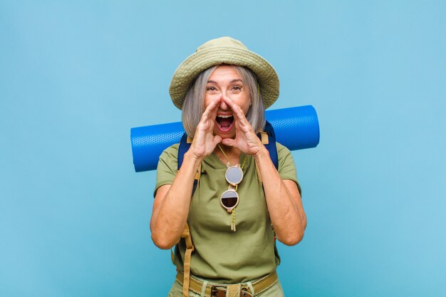 Middle age woman feeling happy, excited and positive, giving a big shout out with hands next to mouth, calling out