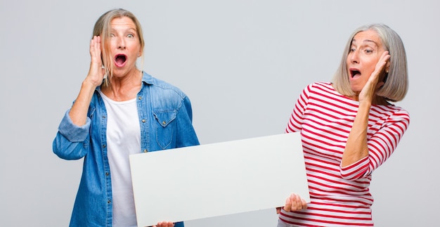 Middle age woman feeling happy, excited and surprised, looking to the side with both hands on face