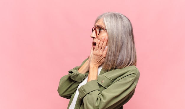 Middle age woman feeling happy, excited and surprised, looking to the side with both hands on face