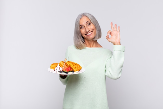 Middle age woman feeling happy, relaxed and satisfied, showing approval with okay gesture, smiling. breakfast concept