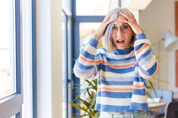 恐怖とショックを感じ、手を頭に上げ、間違いでパニックに陥る中年女性