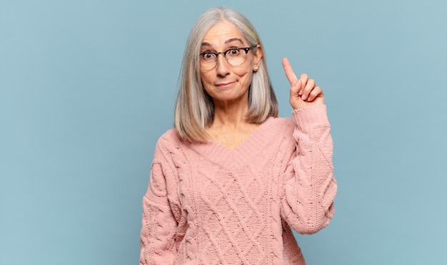 Middle age woman feeling like a genius holding finger proudly up in the air after realizing a great idea, saying eureka