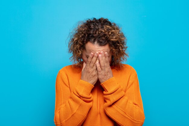 Middle age woman feeling sad, frustrated, nervous and depressed, covering face with both hands, crying