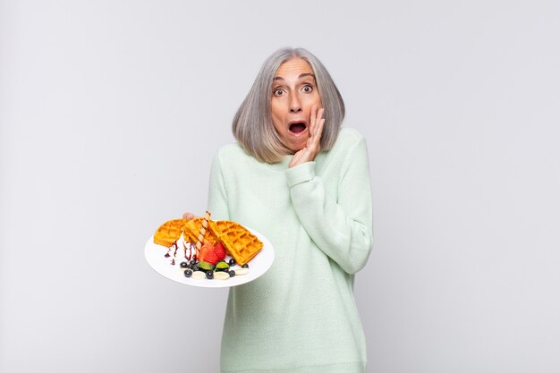 middle age woman feeling shocked and scared, looking terrified with open mouth and hands on cheeks. breakfast concept