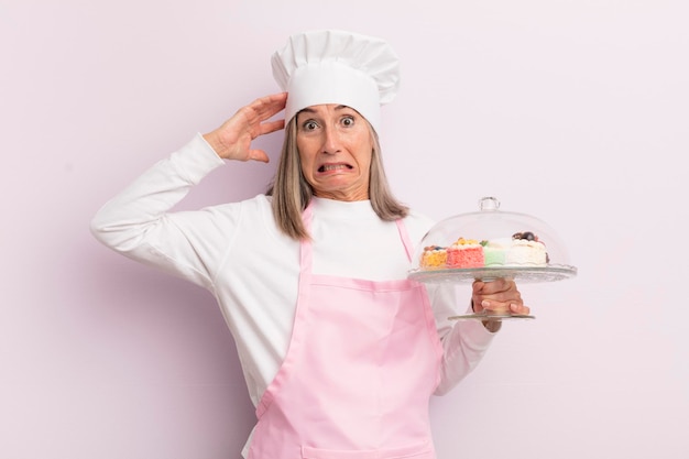 Middle age woman feeling stressed anxious or scared with hands on head baker and cakes concept