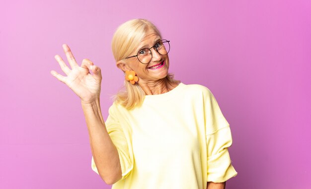 Middle age woman feeling successful and satisfied, smiling with mouth wide open, making okay sign with hand