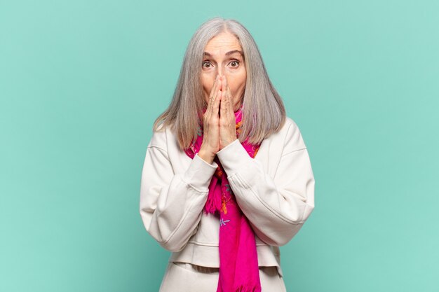 Middle age woman feeling worried, upset and scared, covering mouth with hands, looking anxious and having messed up