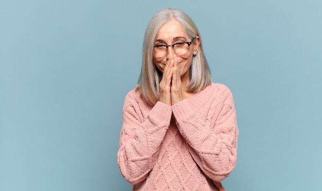 Middle age woman happy and excited, surprised and amazed covering mouth with hands, giggling with a cute expression