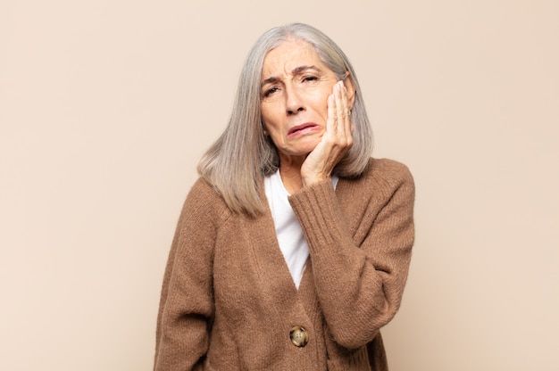 Middle age woman holding cheek and suffering painful toothache