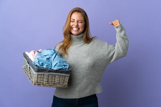 強いジェスチャーをしている紫色の壁に隔離された服のバスケットを保持している中年女性