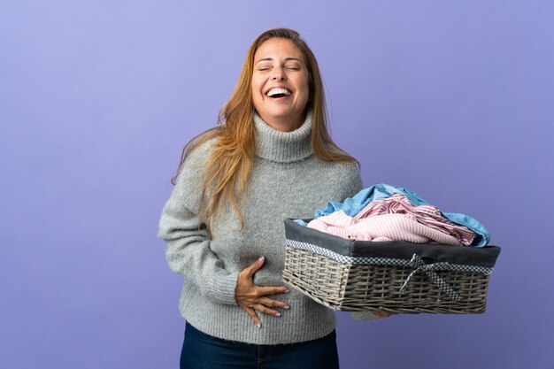 많이 웃 고 보라색 벽에 고립 된 옷 바구니를 들고 중 년 여자