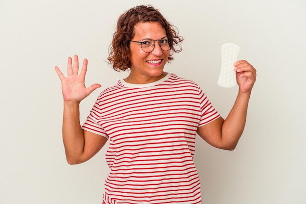 白い背景で隔離の湿布を保持している中年の女性は、指で5番を示して陽気に笑っています。