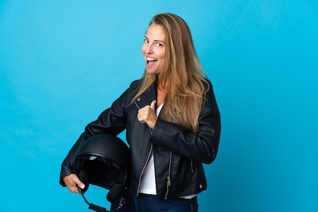 Middle age woman holding a motorcycle helmet isolated on blue proud and self-satisfied