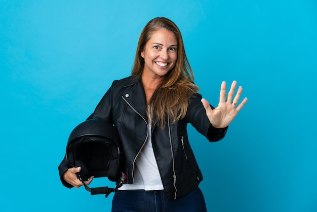 손가락으로 5 세 파란색 벽에 고립 된 오토바이 헬멧을 들고 중년 여자
