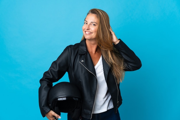 Middle age woman holding a motorcycle helmet isolated on blue wall having doubts