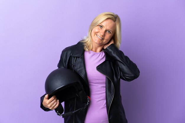 Middle age woman holding a motorcycle helmet isolated on purple laughing