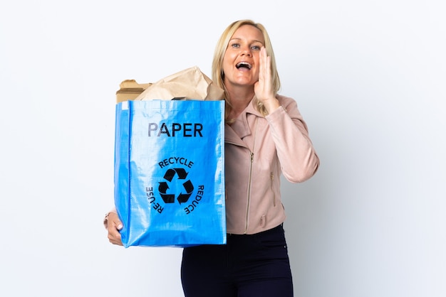 Middle age woman holding a recycling bag full of paper to recycle isolated on white shouting with mouth wide open