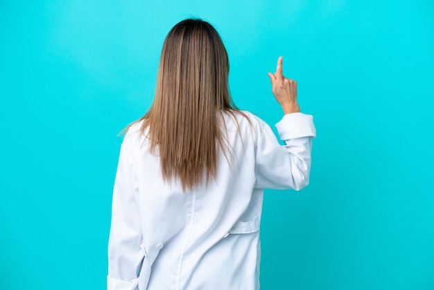 Middle age woman isolated on blue background wearing a doctor gown and pointing back
