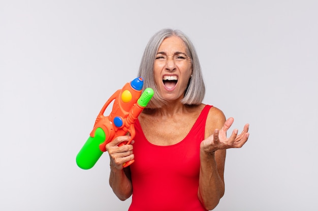 Женщина среднего возраста выглядит сердитой, раздраженной и разочарованной, кричит, черт возьми, или что с тобой не так с водяным пистолетом