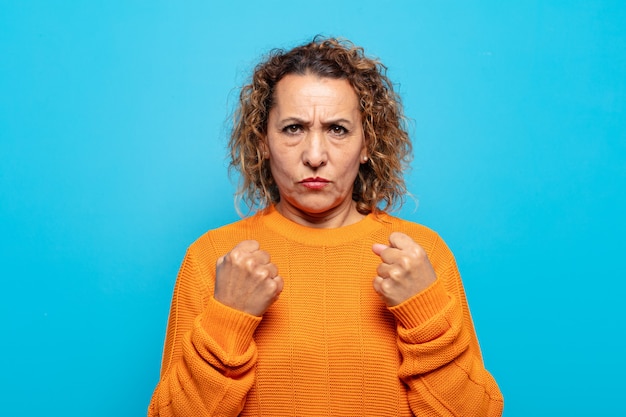 Middle age woman looking confident, angry, strong and aggressive, with fists ready to fight in boxing position