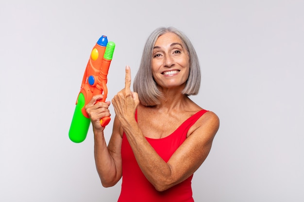 Middle age woman looking excited and surprised pointing to the side and upwards to copy space with a water gun