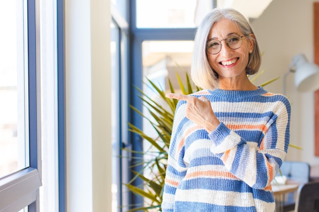 Middle age woman looking excited and surprised pointing to the side and upwards to copy space