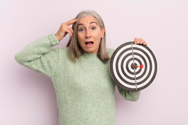 Middle age woman looking happy astonished and surprised darts target concept