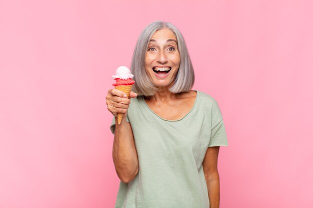 Middle age woman looking happy and pleasantly surprised, excited with a fascinated and shocked expression having an ice cream