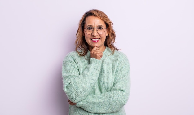 Middle age woman looking happy and smiling with hand on chin, wondering or asking a question, comparing options