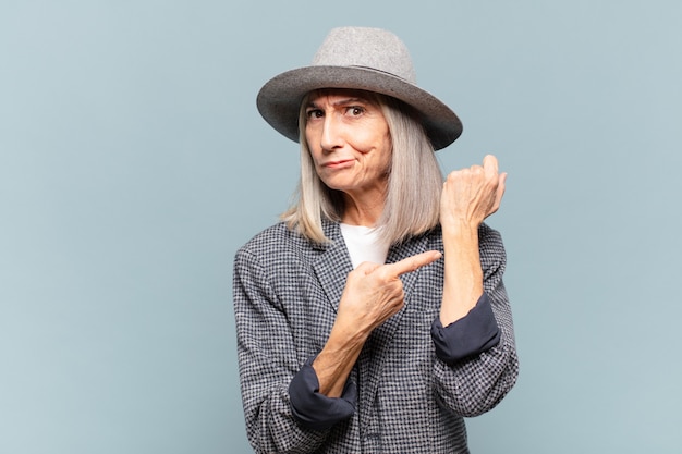 Photo middle age woman looking impatient and angry, pointing at watch, asking for punctuality, wants to be on time