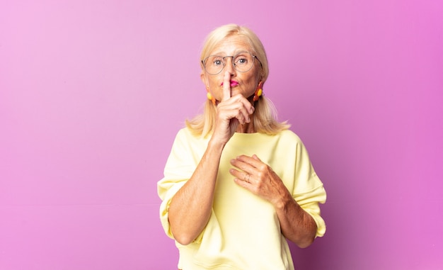 Middle age woman looking serious and cross with finger pressed to lips demanding silence or quiet, keeping a secret