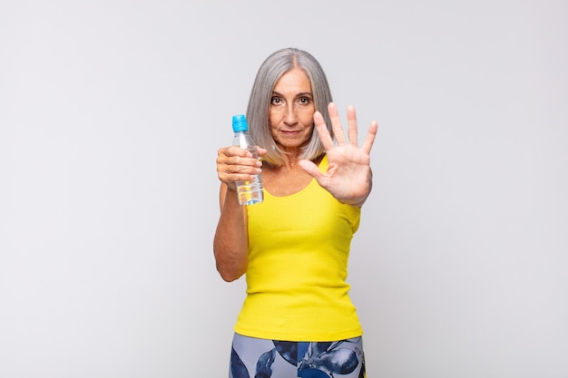 middle age woman looking serious, stern, displeased and angry showing open palm making stop gesture. fitness concept