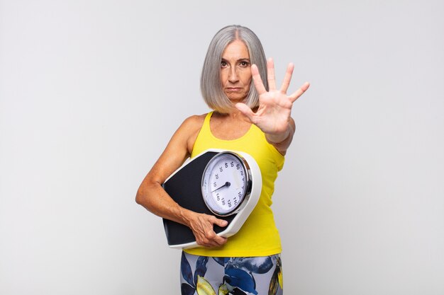 Middle age woman looking serious, stern, displeased and angry showing open palm making stop gesture. fitness concept