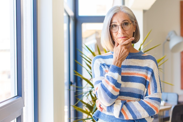 Middle age woman looking serious, thoughtful and distrustful, with one arm crossed and hand on chin, weighting options