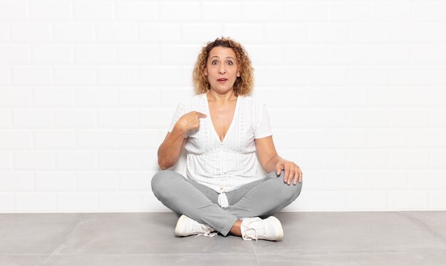 middle age woman looking shocked and surprised with mouth wide open, pointing to self