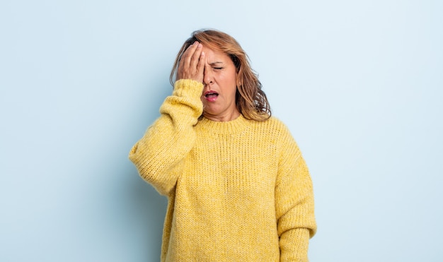 Middle age woman looking sleepy, bored and yawning, with a headache and one hand covering half the face