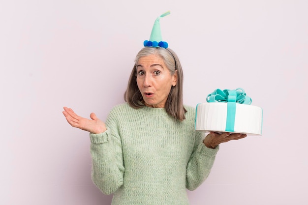 Middle age woman looking surprised and shocked with jaw dropped holding an object bitrthday cake concept