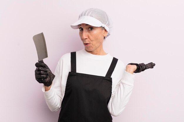 Middle age woman looking surprised and shocked with jaw dropped holding an object butcher concept