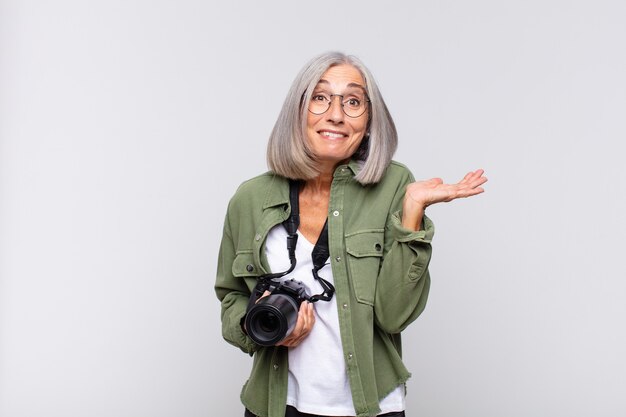 Middle age woman looking surprised and shocked, with jaw\
dropped holding an object with an open hand on the side.\
photographer concept