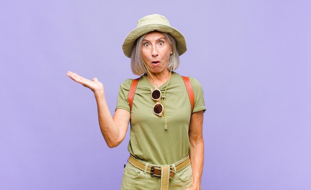 Middle age woman looking surprised and shocked, with jaw dropped holding an object with an open hand on the side