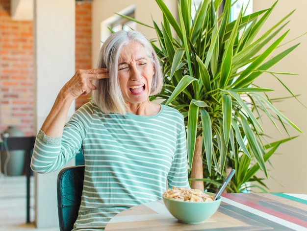 Middle age woman looking unhappy and stressed, suicide gesture making gun sign with hand, pointing to head