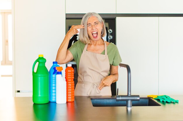 Middle age woman looking unhappy and stressed, suicide gesture making gun sign with hand, pointing to head