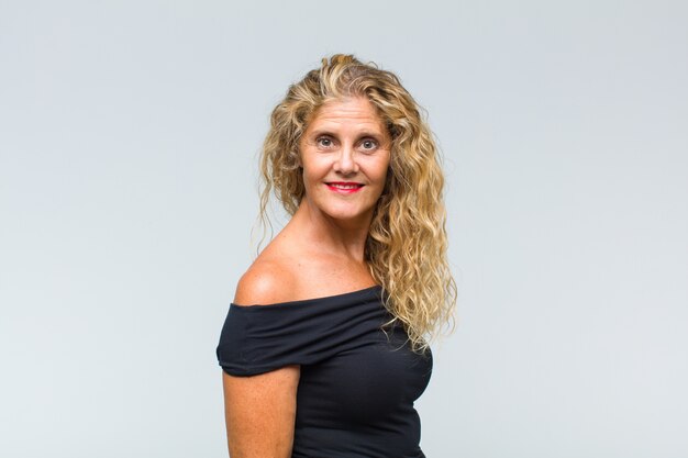 Middle age woman posing and looking to camera against white wall