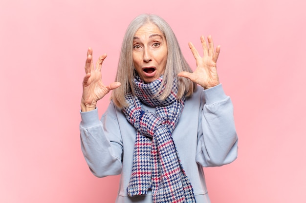 Middle age woman screaming with hands up in the air, feeling furious, frustrated, stressed and upset