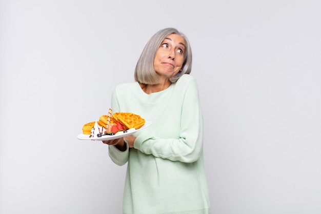 Middle age woman shrugging, feeling confused and uncertain, doubting with arms crossed and puzzled look. breakfast concept