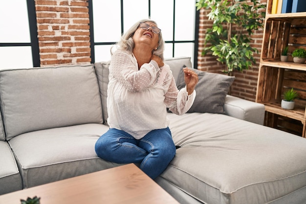 Middle age woman sitting on sofa suffering for back pain at home