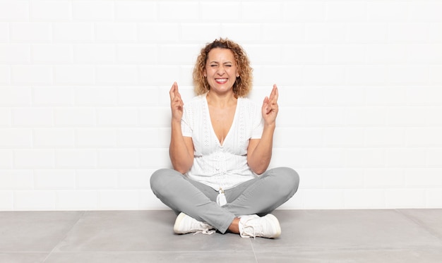 Foto donna di mezza età sorridente e incrociando ansiosamente entrambe le dita, preoccupata e desiderando o sperando buona fortuna